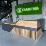 Nowoczesna lada recepcyjna z drewnianym blatem i geometrycznym frontem w industrialnym wnętrzu